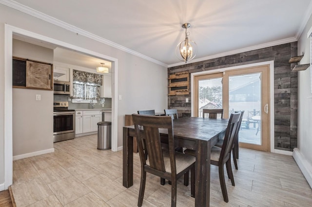 dining space with an inviting chandelier, sink, ornamental molding, and wood walls