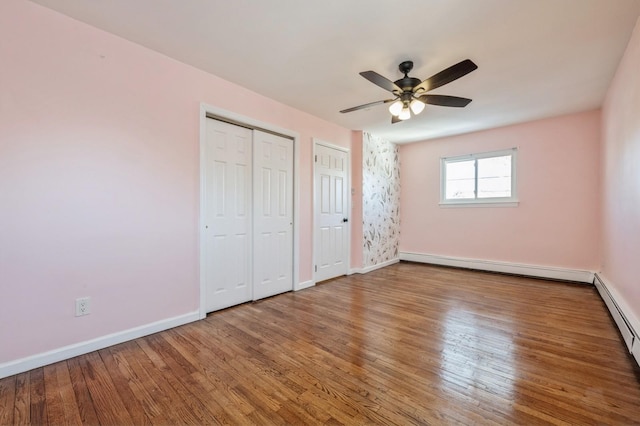 unfurnished bedroom with multiple closets, a baseboard radiator, hardwood / wood-style floors, and ceiling fan