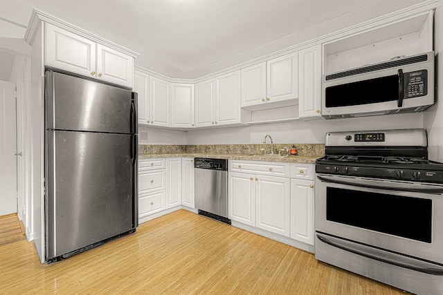 kitchen featuring sink, appliances with stainless steel finishes, white cabinetry, light stone counters, and light hardwood / wood-style floors