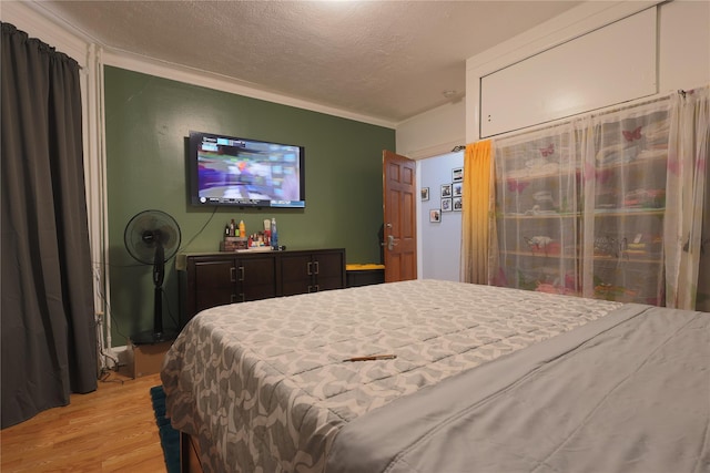 bedroom with crown molding, a textured ceiling, and light hardwood / wood-style flooring