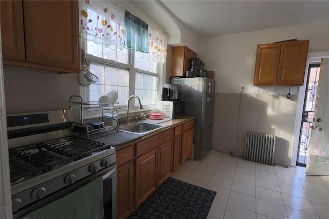 kitchen featuring sink, radiator heating unit, light tile patterned flooring, and appliances with stainless steel finishes