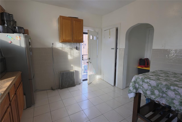 kitchen featuring light tile patterned floors, radiator heating unit, and stainless steel refrigerator