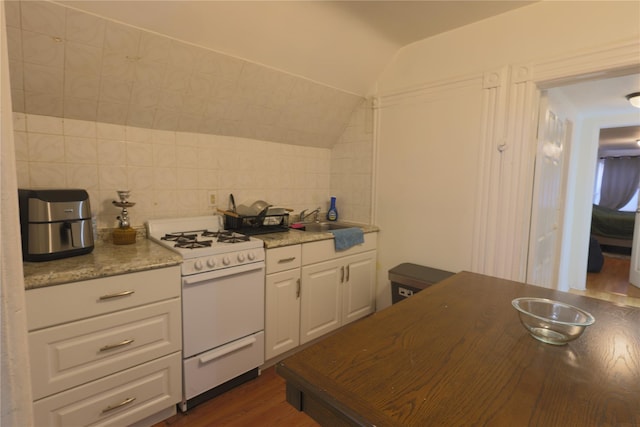 kitchen with lofted ceiling, white gas range oven, tile walls, white cabinets, and decorative backsplash