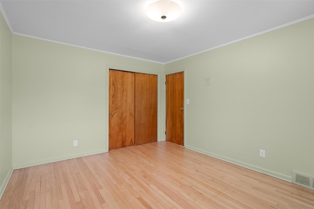 unfurnished bedroom featuring crown molding, a closet, and light wood-type flooring