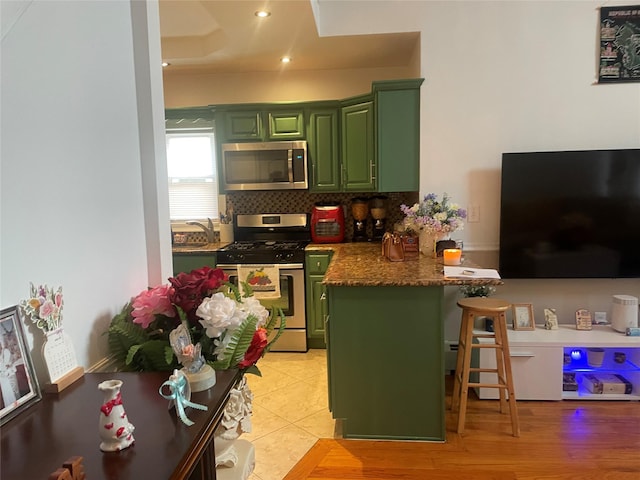 kitchen with a kitchen bar, stainless steel appliances, kitchen peninsula, and green cabinets