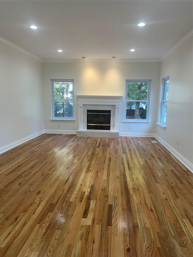 unfurnished living room featuring a healthy amount of sunlight, ornamental molding, and light hardwood / wood-style flooring