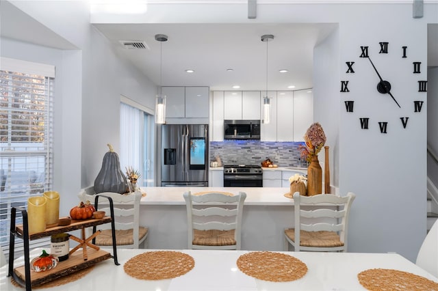 kitchen with a breakfast bar area, white cabinets, pendant lighting, stainless steel appliances, and backsplash