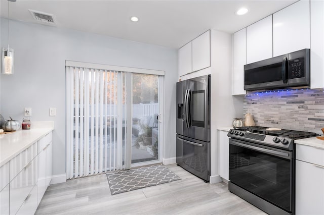 kitchen featuring appliances with stainless steel finishes, pendant lighting, white cabinets, and light hardwood / wood-style floors