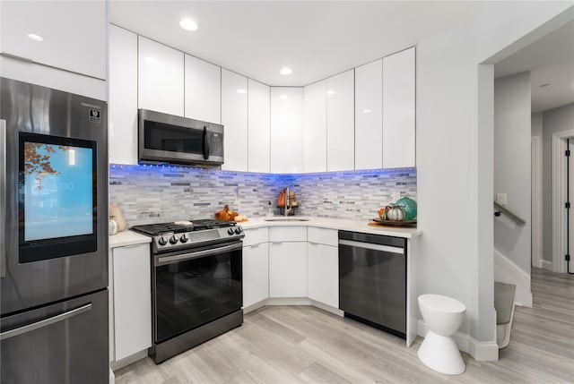 kitchen with sink, light wood-type flooring, stainless steel appliances, decorative backsplash, and white cabinets