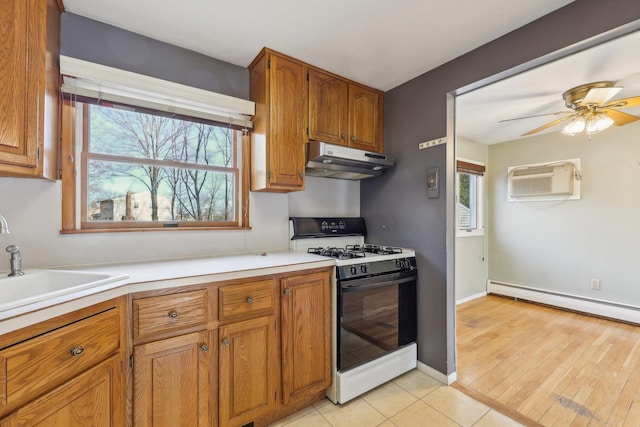 kitchen with under cabinet range hood, brown cabinetry, baseboard heating, and range with gas cooktop