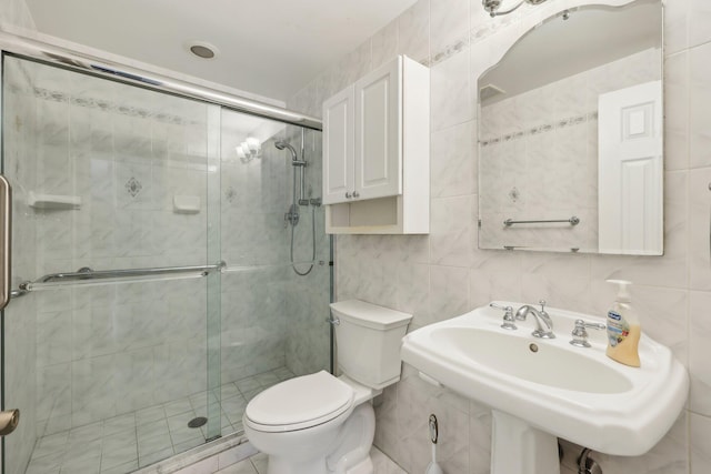 bathroom featuring toilet, a sink, a shower stall, and tile walls