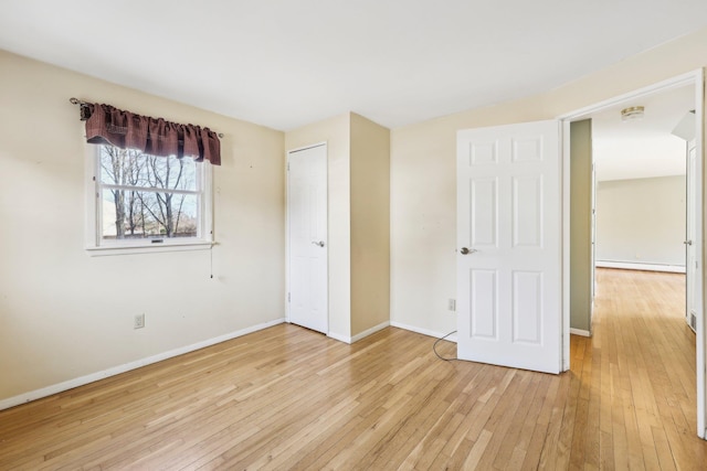 unfurnished bedroom featuring a baseboard heating unit, light wood-type flooring, and baseboards