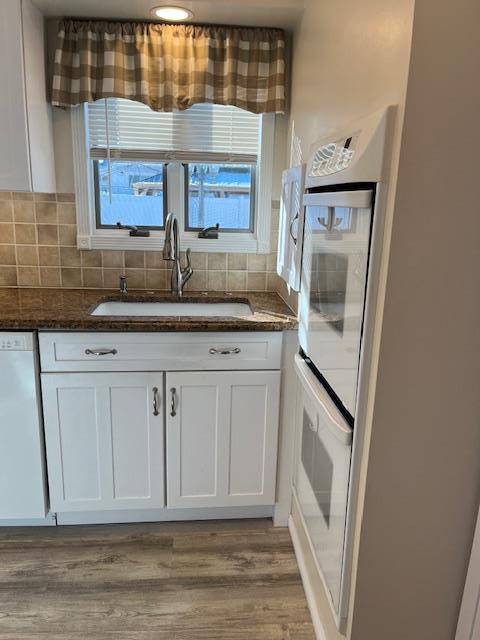 kitchen with tasteful backsplash, white cabinetry, sink, dark stone countertops, and white appliances