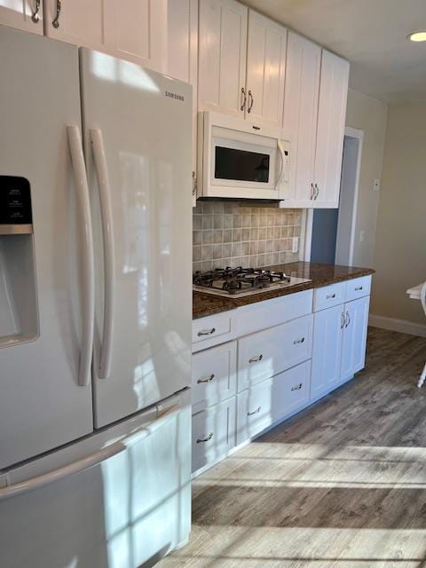 kitchen with white appliances, light hardwood / wood-style flooring, dark stone countertops, white cabinets, and decorative backsplash