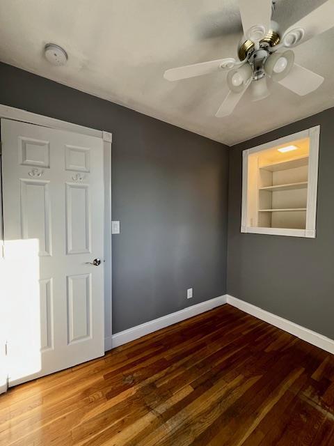 empty room with hardwood / wood-style floors, ceiling fan, and built in shelves