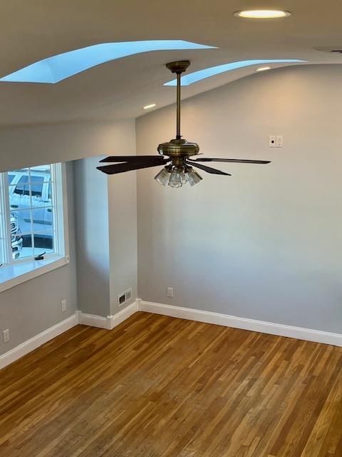 unfurnished room featuring lofted ceiling with skylight, hardwood / wood-style floors, and ceiling fan