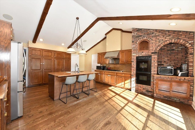 kitchen with appliances with stainless steel finishes, dark hardwood / wood-style floors, a center island with sink, and vaulted ceiling with beams