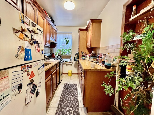 kitchen with tasteful backsplash, gas stove, white fridge, and light tile patterned flooring