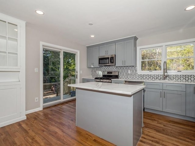 kitchen with appliances with stainless steel finishes, tasteful backsplash, light stone counters, a kitchen island, and dark hardwood / wood-style flooring