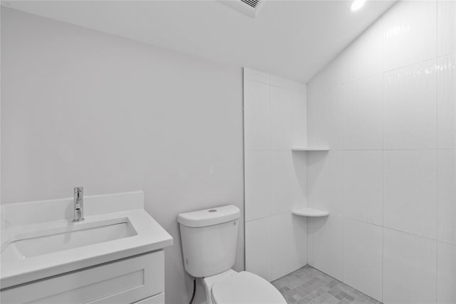 bathroom with a tile shower, toilet, vanity, and lofted ceiling