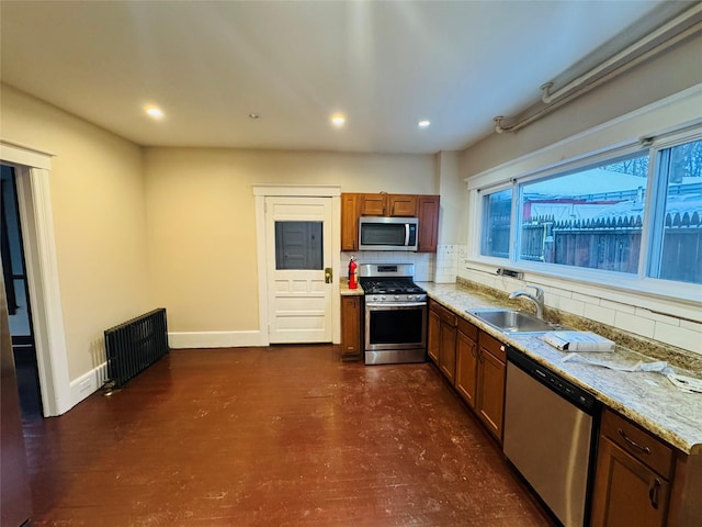 kitchen featuring sink, radiator, backsplash, stainless steel appliances, and light stone counters