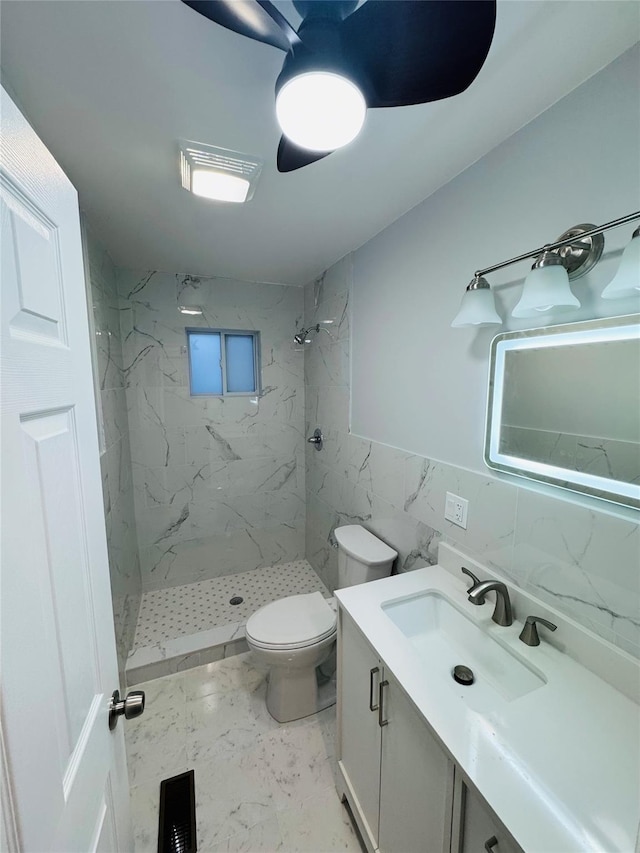 bathroom with vanity, a tile shower, tile walls, and toilet