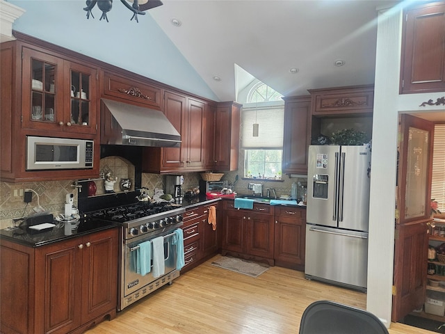 kitchen featuring vaulted ceiling, appliances with stainless steel finishes, range hood, decorative backsplash, and light hardwood / wood-style floors