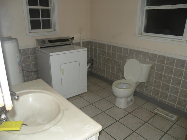 bathroom with water heater, washer / dryer, tile walls, toilet, and tile patterned floors