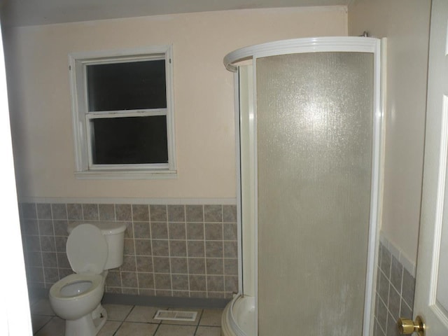 bathroom with tile walls, a shower with door, tile patterned floors, and toilet