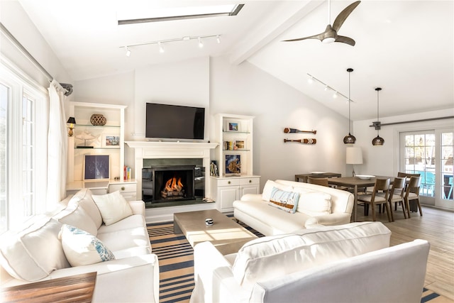 living room featuring lofted ceiling with beams, rail lighting, ceiling fan, and light wood-type flooring