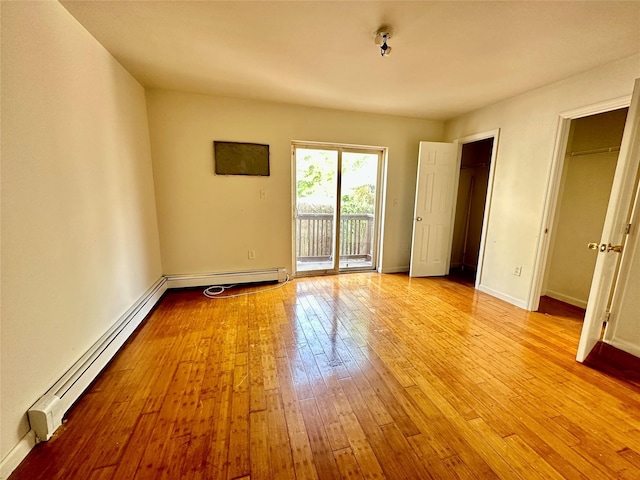 unfurnished room with baseboard heating, hardwood / wood-style flooring, and baseboards