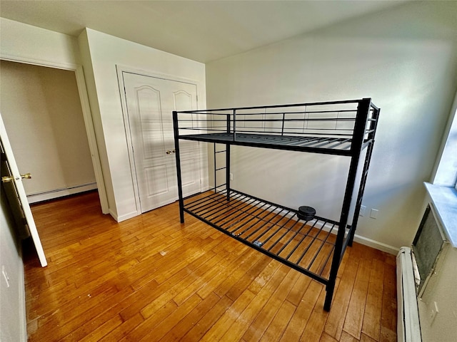 bedroom with a baseboard heating unit, wood-type flooring, and baseboards