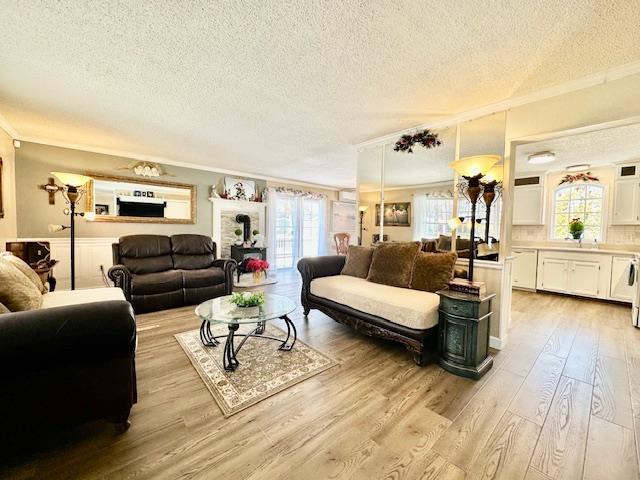 living room featuring crown molding, a healthy amount of sunlight, a textured ceiling, and light wood-type flooring