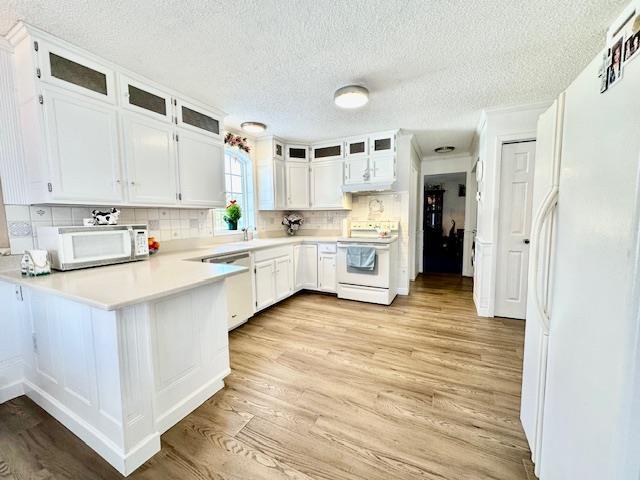 kitchen featuring backsplash, white cabinets, light hardwood / wood-style floors, kitchen peninsula, and white appliances