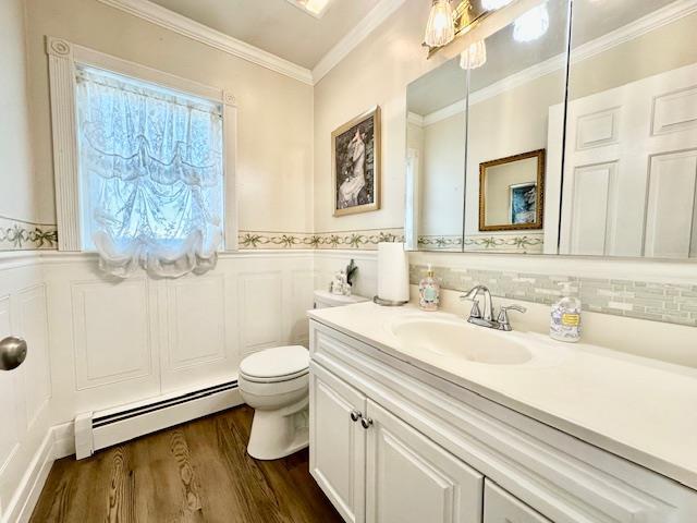 bathroom featuring toilet, wood-type flooring, ornamental molding, vanity, and a baseboard heating unit