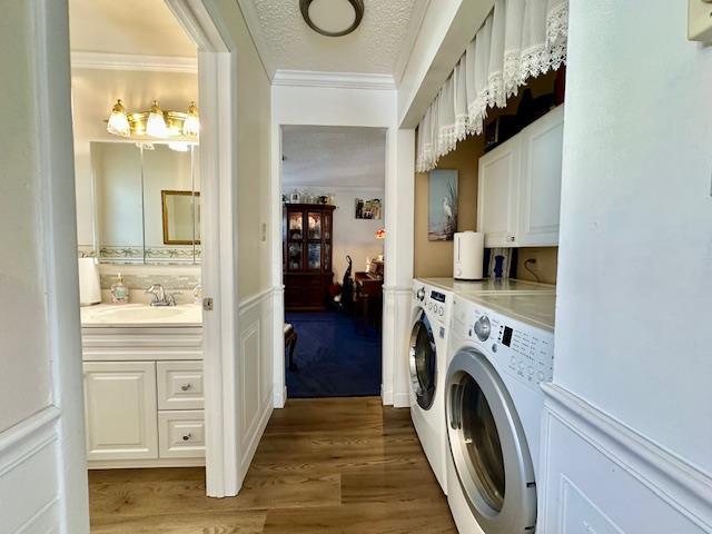 washroom featuring sink, cabinets, hardwood / wood-style flooring, washing machine and clothes dryer, and a textured ceiling