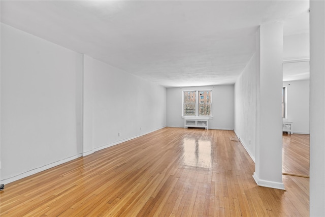 unfurnished room featuring radiator, light wood-style flooring, and baseboards