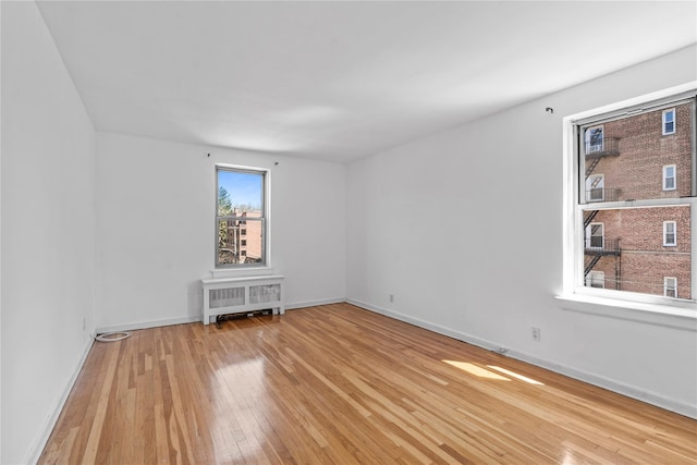 spare room with radiator, wood-type flooring, and baseboards