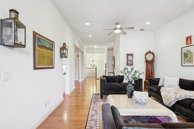 living room with ceiling fan with notable chandelier, ornamental molding, and light wood-type flooring