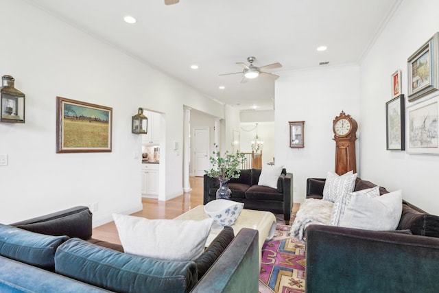 living room with crown molding, ceiling fan with notable chandelier, and light wood-type flooring