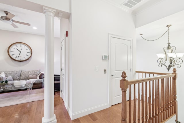 corridor with an inviting chandelier, crown molding, light wood-type flooring, and ornate columns