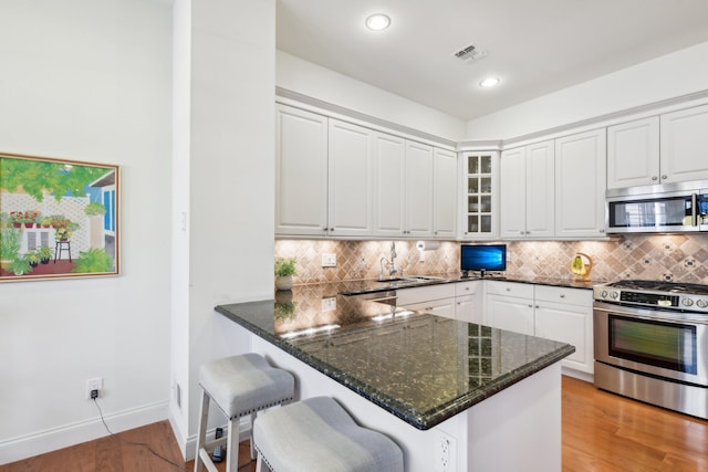 kitchen with appliances with stainless steel finishes, kitchen peninsula, a breakfast bar area, and white cabinets