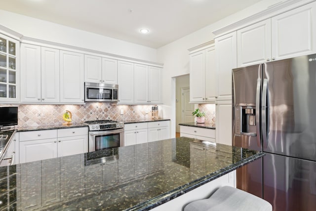 kitchen with white cabinetry, decorative backsplash, stainless steel appliances, and dark stone countertops