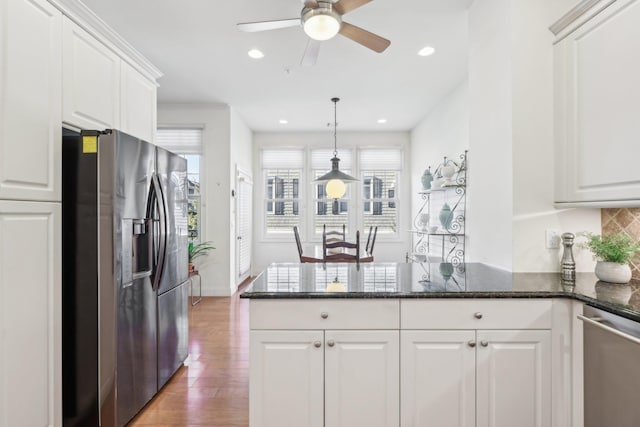 kitchen with appliances with stainless steel finishes, white cabinets, dark stone counters, light hardwood / wood-style floors, and backsplash