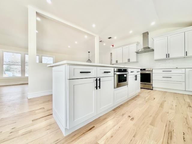 kitchen with white cabinetry, wall chimney range hood, a kitchen island, stainless steel appliances, and backsplash