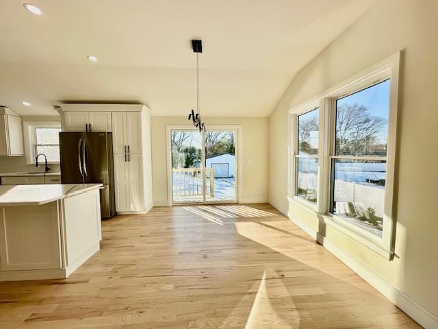 interior space featuring black refrigerator, decorative light fixtures, white cabinetry, sink, and light wood-type flooring