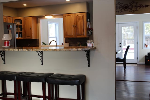 kitchen featuring a breakfast bar, light stone counters, stainless steel refrigerator, dark hardwood / wood-style floors, and kitchen peninsula