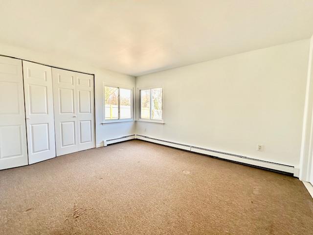 unfurnished bedroom featuring carpet floors, a baseboard radiator, and a closet