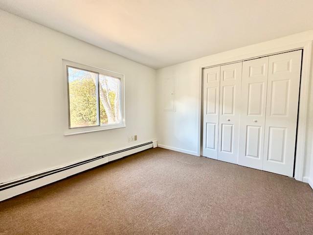 unfurnished bedroom featuring carpet flooring, baseboard heating, and a closet