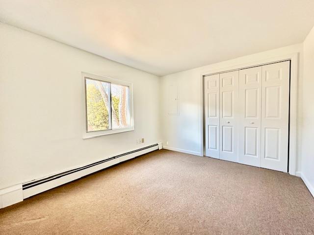 unfurnished bedroom with carpet flooring, a closet, and baseboard heating